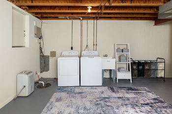 A laundry room with a washer and dryer, a rug, and a trash can.